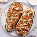 Overhead view of stuffed eggplant on plate next to bowls of tahini and parsley