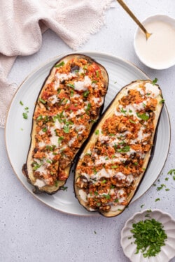 Overhead view of stuffed eggplant on plate next to bowls of tahini and parsley