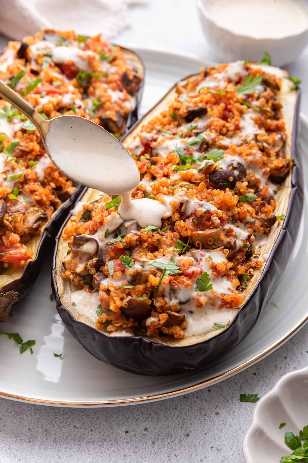 Drizzling tahini sauce over quinoa stuffed eggplant