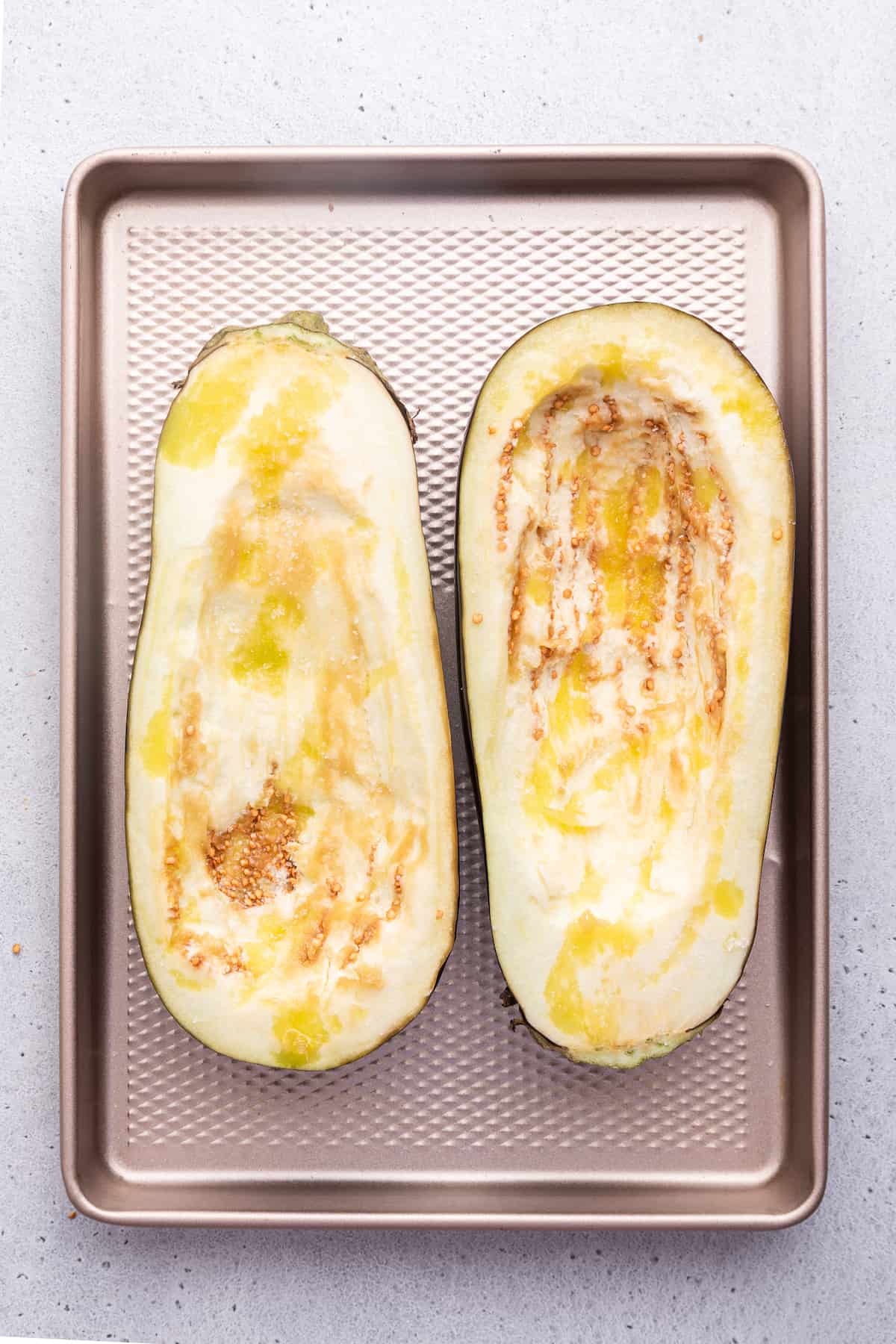 Overhead view of eggplant halves on sheet pan before baking