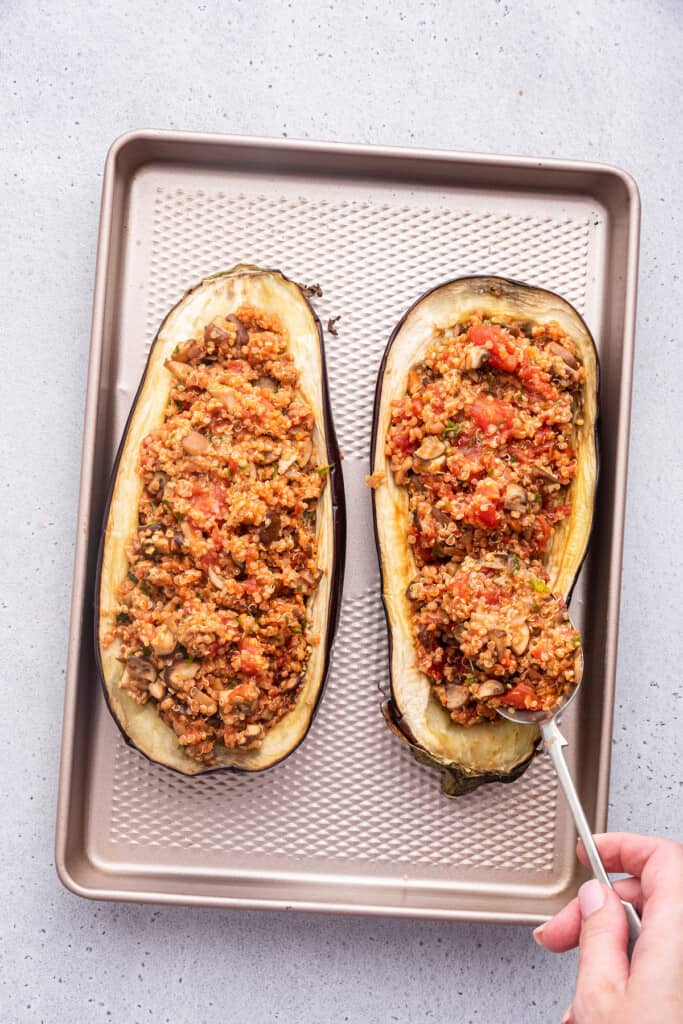 Overhead view of spoon filling eggplant halves with stuffing