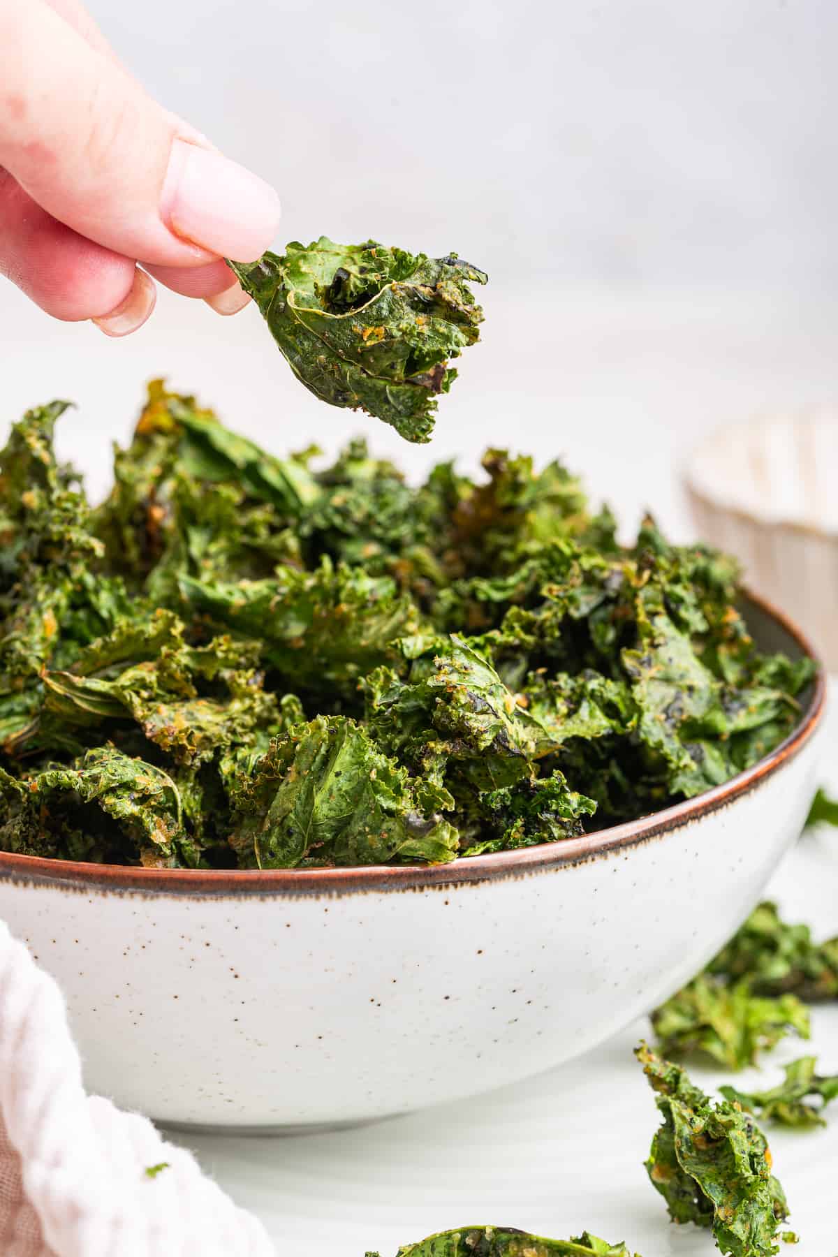 Hand lifting air fryer kale chip out of bowl