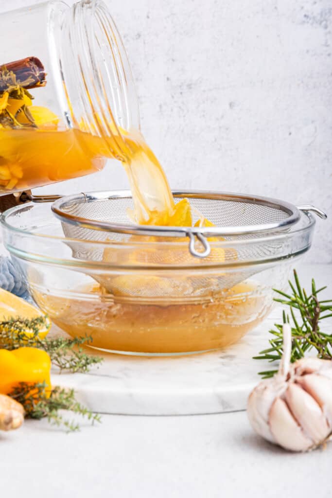 Pouring fire cider through mesh strainer into bowl