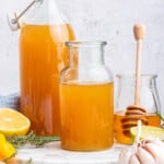 Two bottles of fire cider set next to jar of honey with dipper