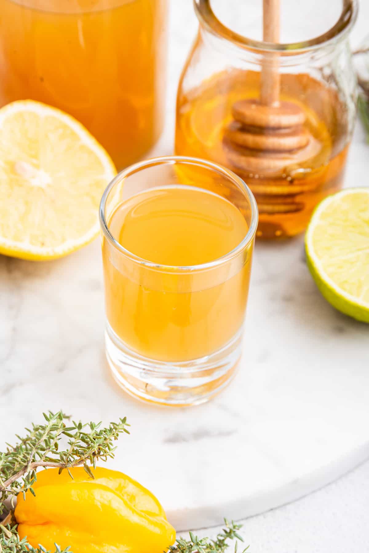 Shot of fire cider with jar of honey, lemon, and lime in background