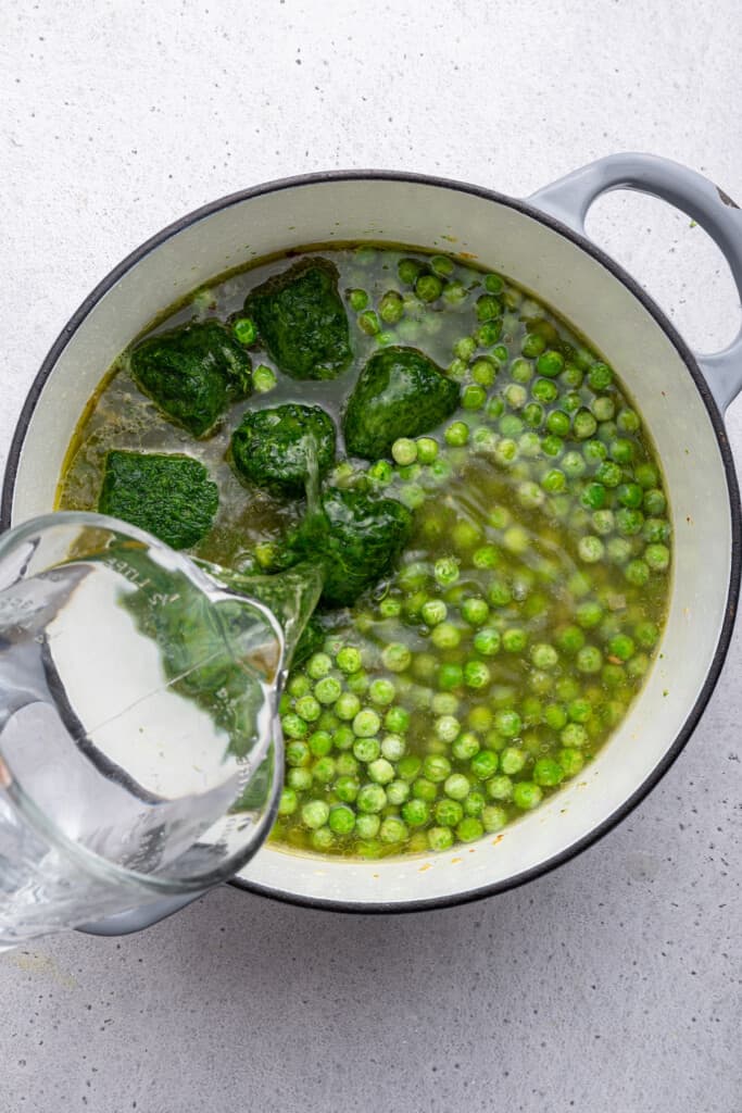 Overhead view of water being poured into pot of soup