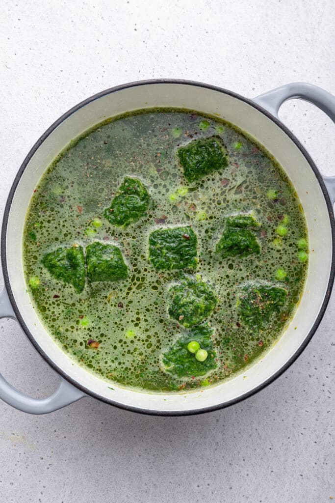 Overhead view of frozen spinach added to pot of soup