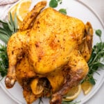 Instant Pot whole chicken on platter with sprigs of fresh herbs and lemons