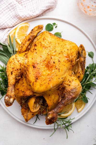 Instant Pot whole chicken on platter with sprigs of fresh herbs and lemons