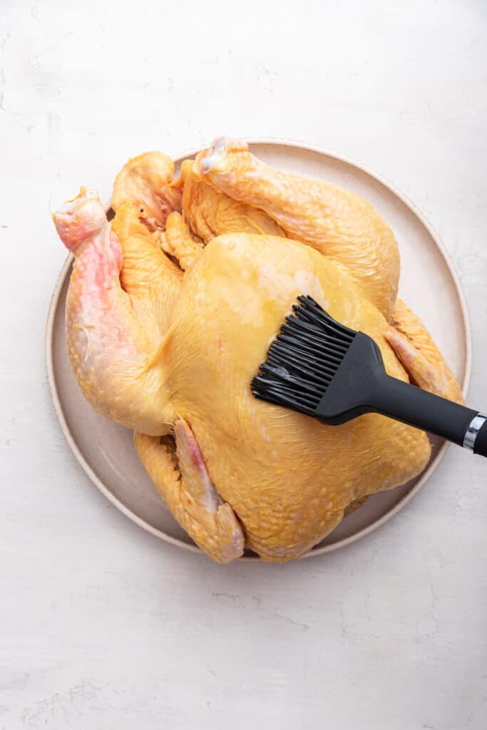 Overhead view of olive oil being brushed onto raw chicken