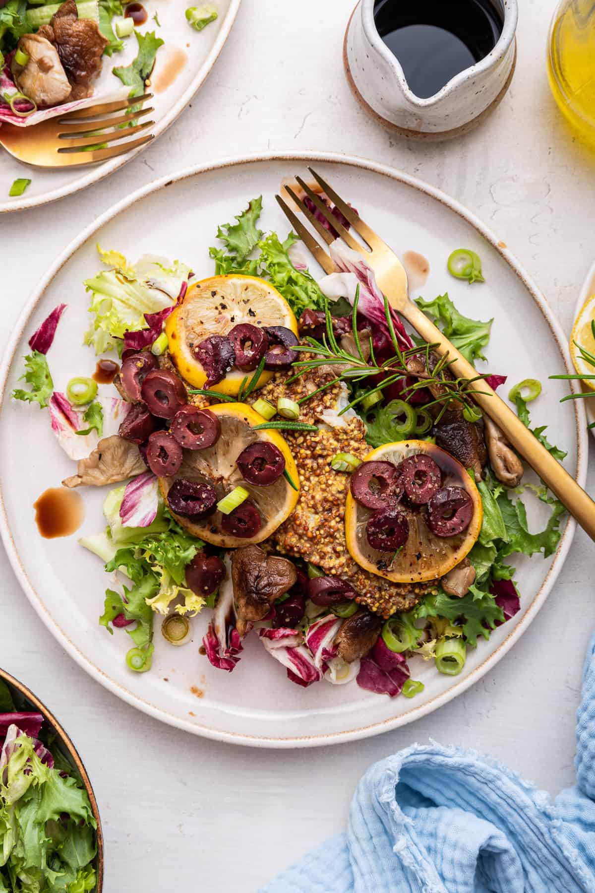 This easy baked halibut will leave you feeling happy and satisfied! Grainy mustard, fresh rosemary, lemon, and olives add big, bold flavors. Overhead view of rosemary and mustard baked halibut with lemon and olives