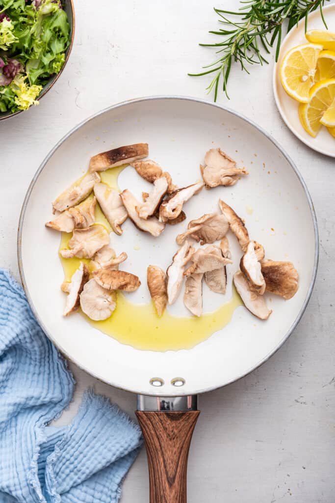 Overhead view of uncooked shiitake mushrooms in skillet with oil