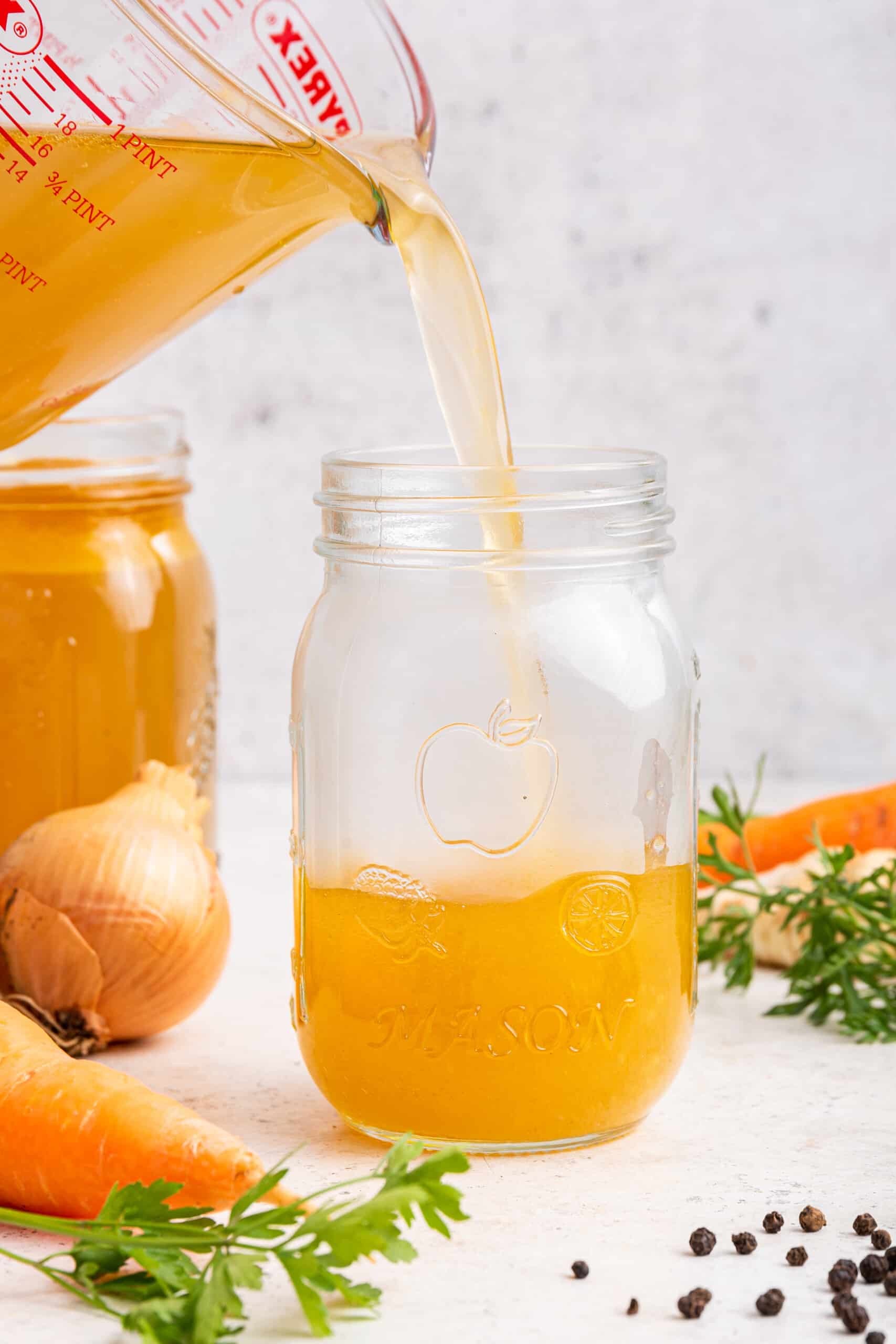 Pouring Instant Pot chicken bone broth from liquid measuring cup into jar