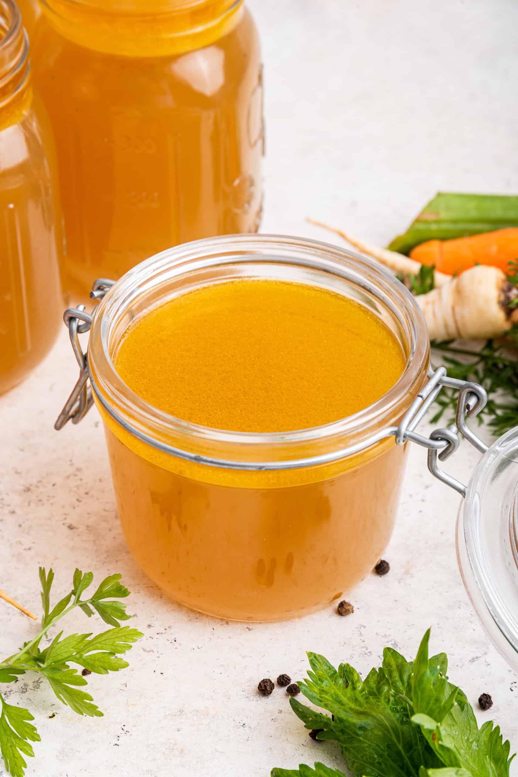 Jar of Instant Pot chicken bone broth with additional jars and vegetables in background