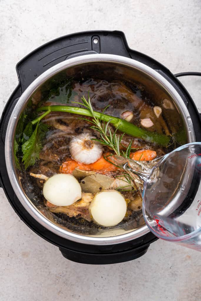 Overhead view of water being poured into Instant Pot for bone broth