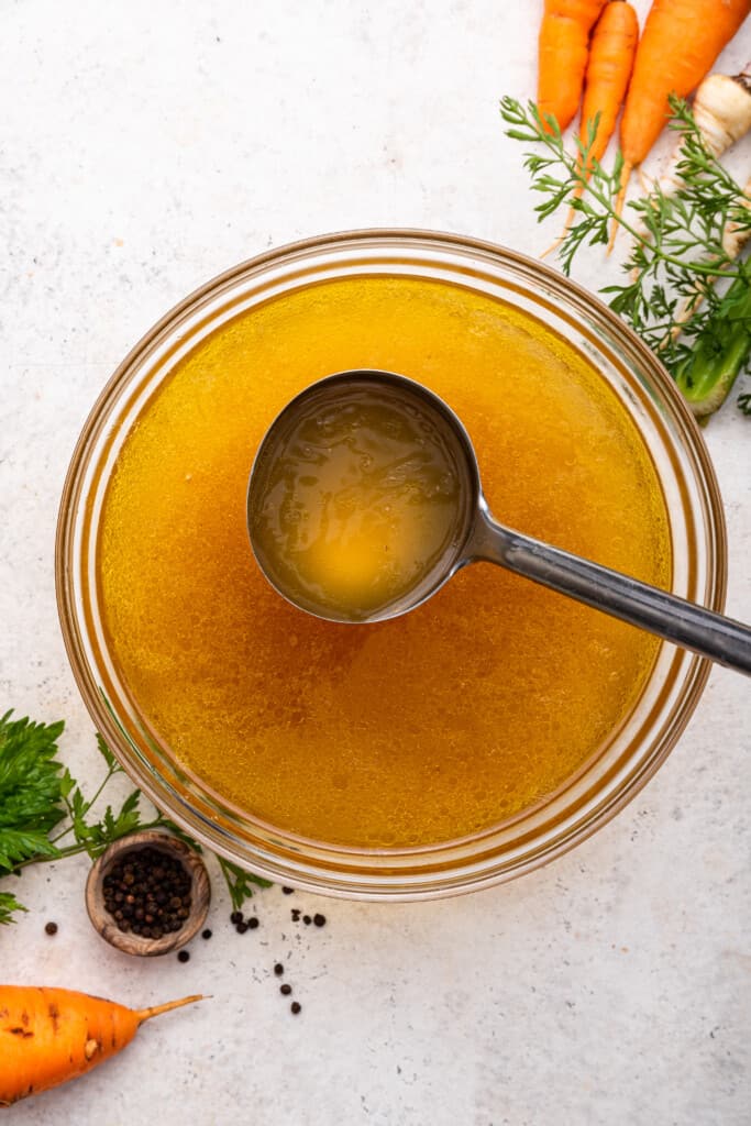 Overhead view of Instant Pot chicken bone broth in glass bowl with ladle