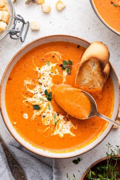 Bowl of roasted red pepper soup with spoon and toasted bread