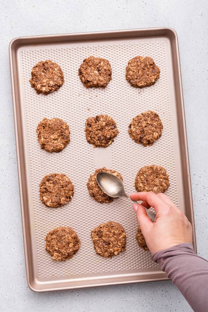 Overhead view showing spoon flattening banana oatmeal cookies before baking