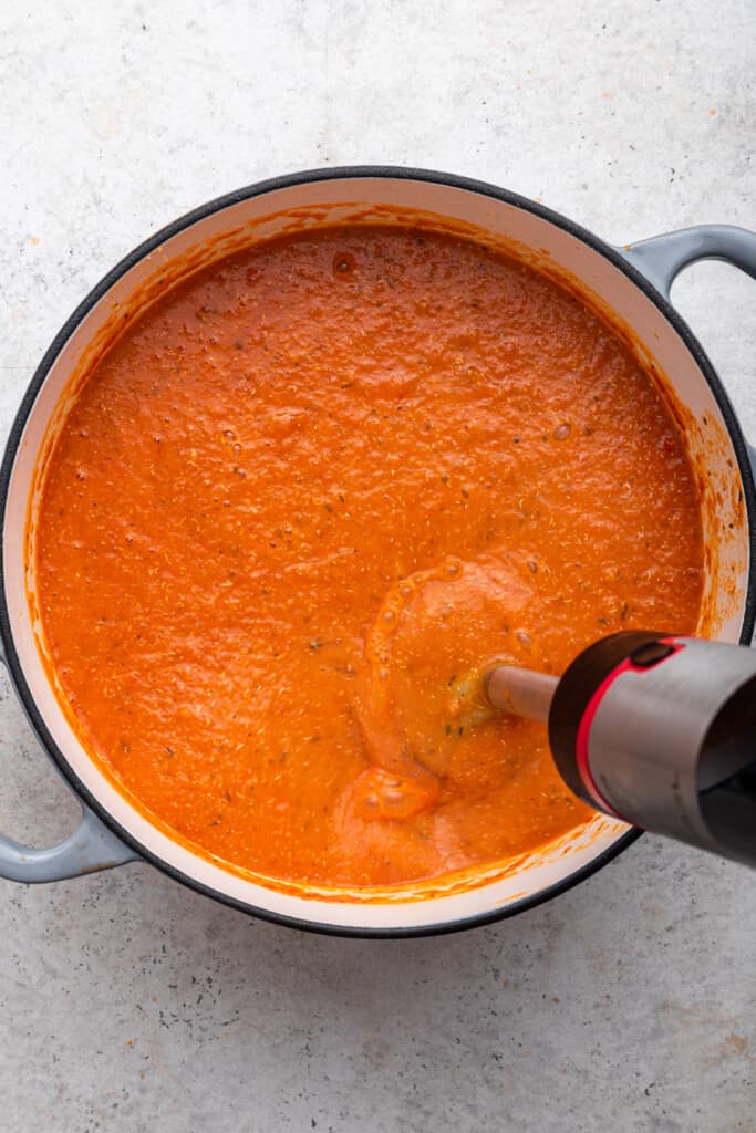 Immersion blender mixing roasted red pepper soup in pot