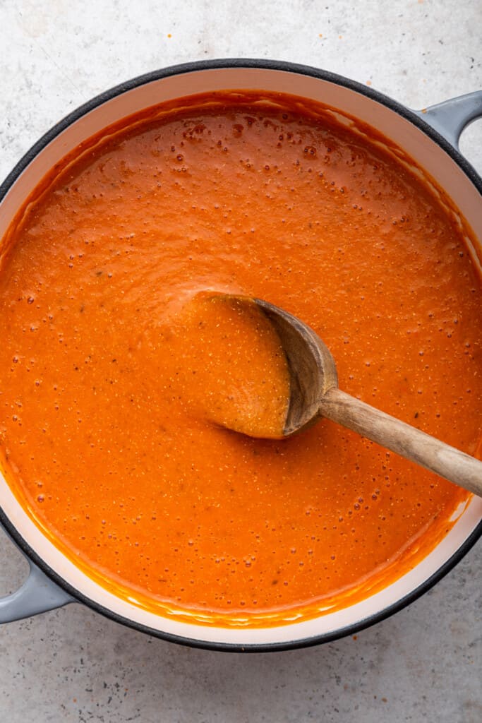 Spoon stirring roasted red pepper soup in Dutch oven