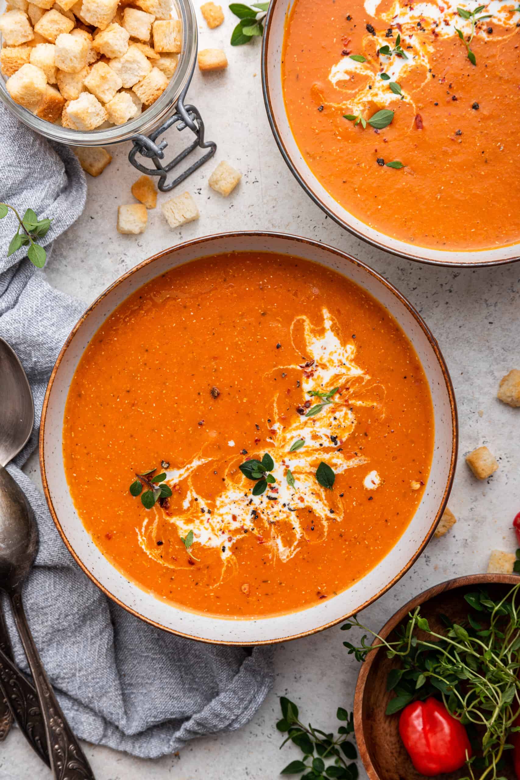 Two bowls of roasted red pepper soup with jar of croutons