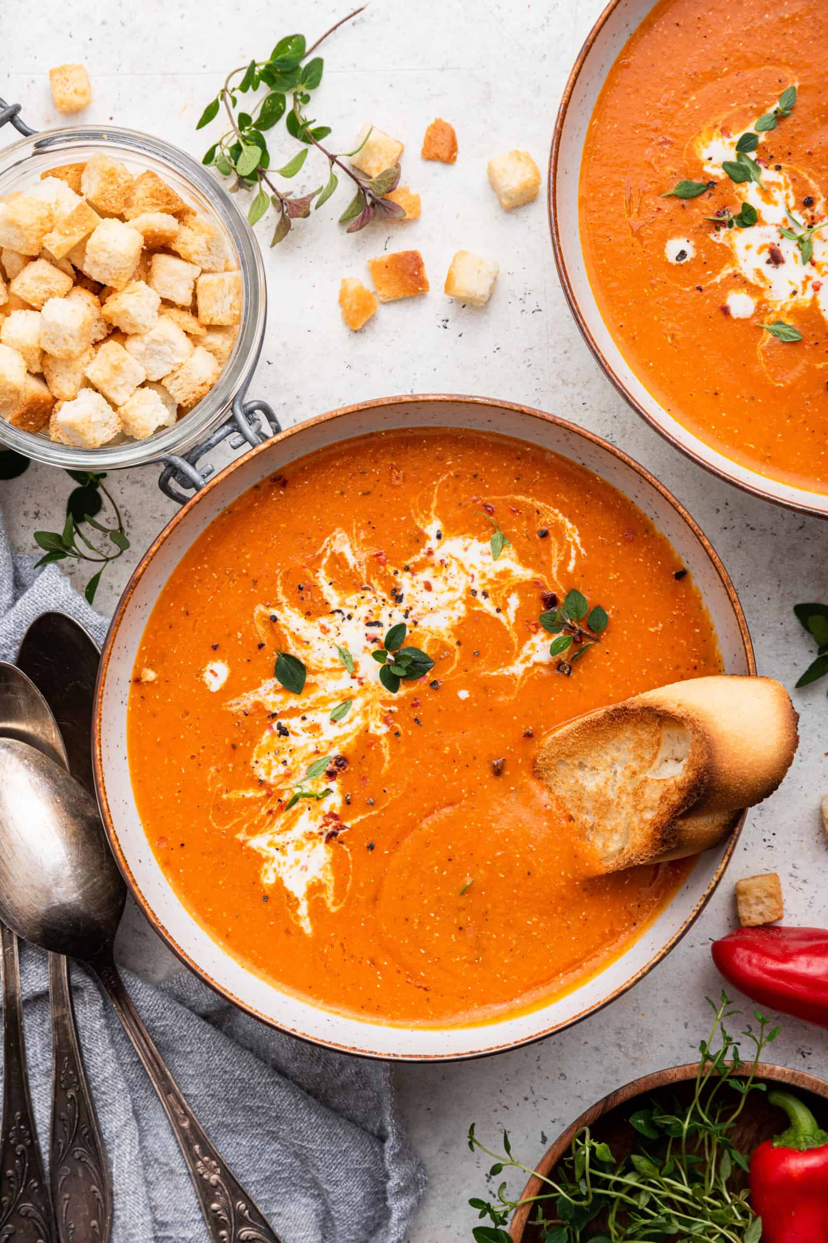 Bowl of roasted red pepper soup garnished with coconut milk, herbs, and toasted bread