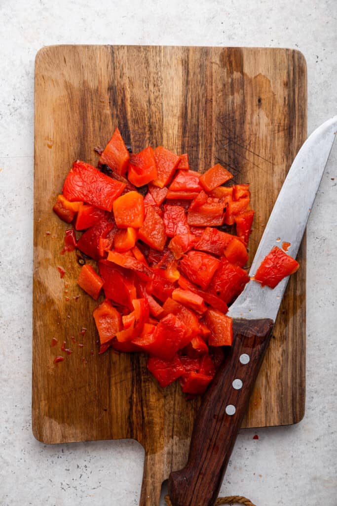 Overhead view of diced roasted red peppers on cutting board with knife