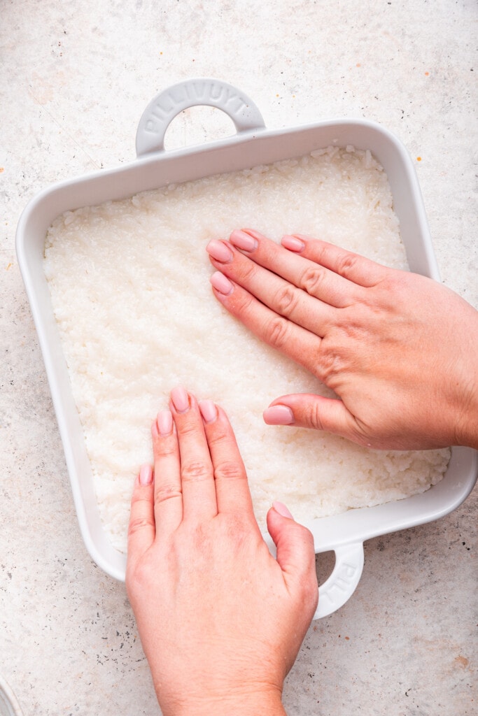 Overhead view of hands pressing sushi rice in casserole dish