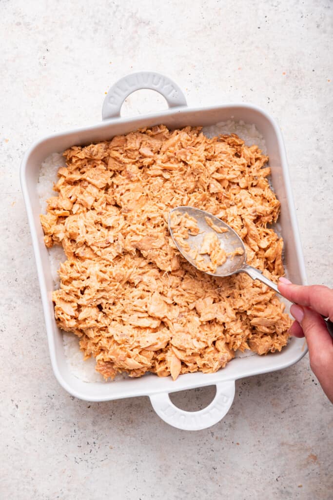 Overhead view of spoon spreading salmon layer on sushi bake