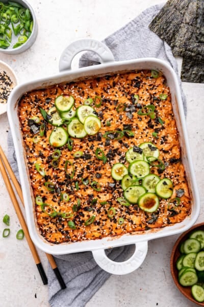 Overhead view of salmon sushi bake in baking dish with sliced cucumbers and green onions for garnish