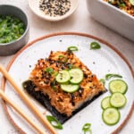 Salmon sushi bake on plate with sliced cucumbers, nori, and green onions