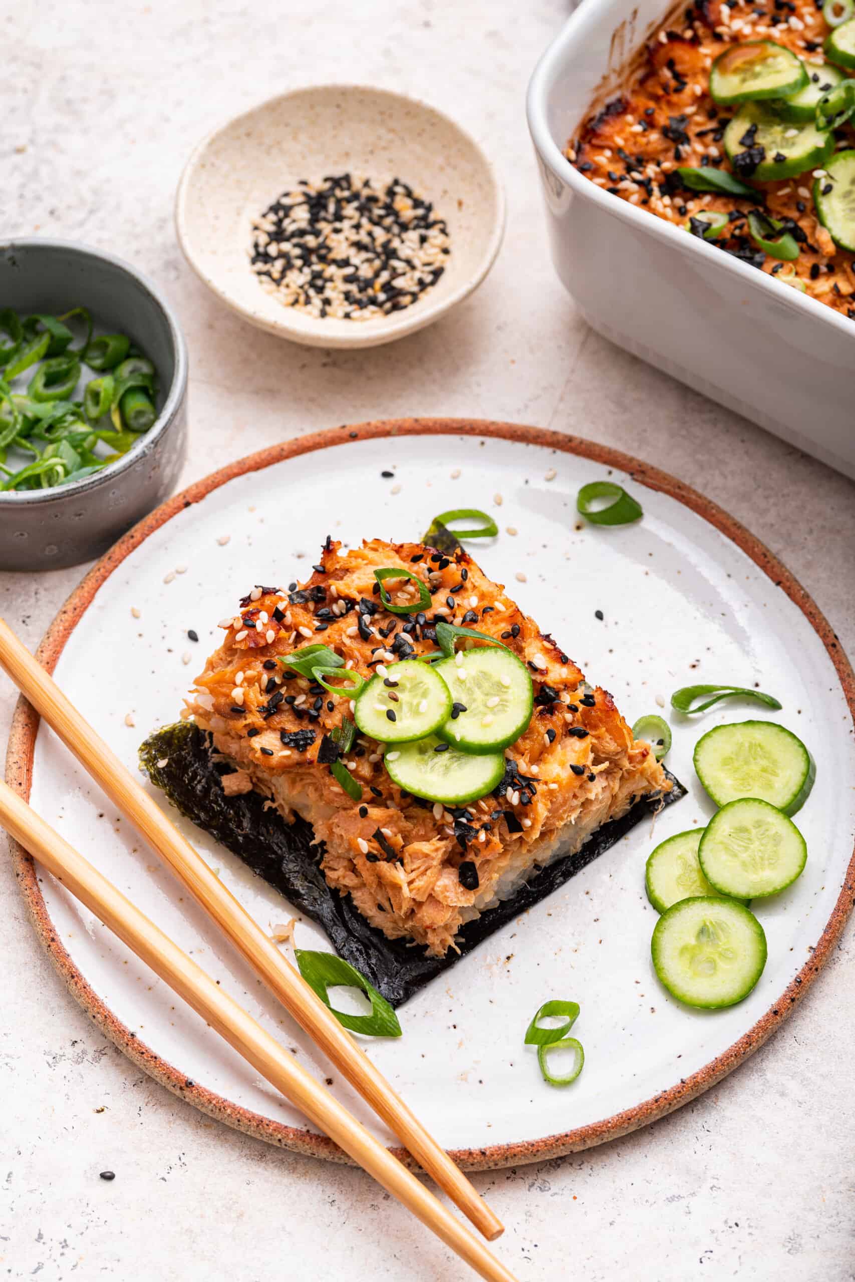 Salmon sushi bake on plate with sliced cucumbers, nori, and green onions