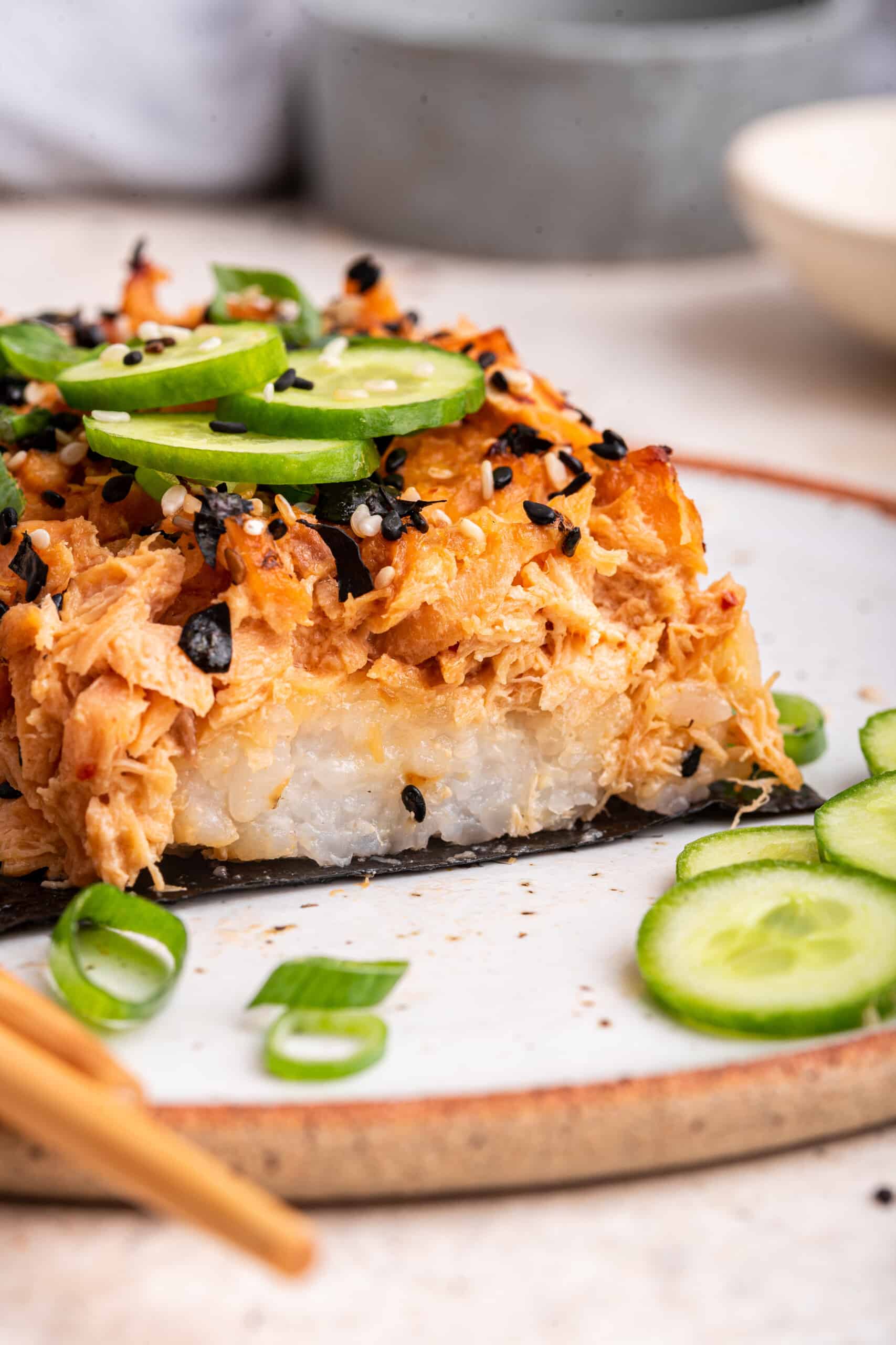 Salmon sushi bake on plate with sliced cucumbers and green onions