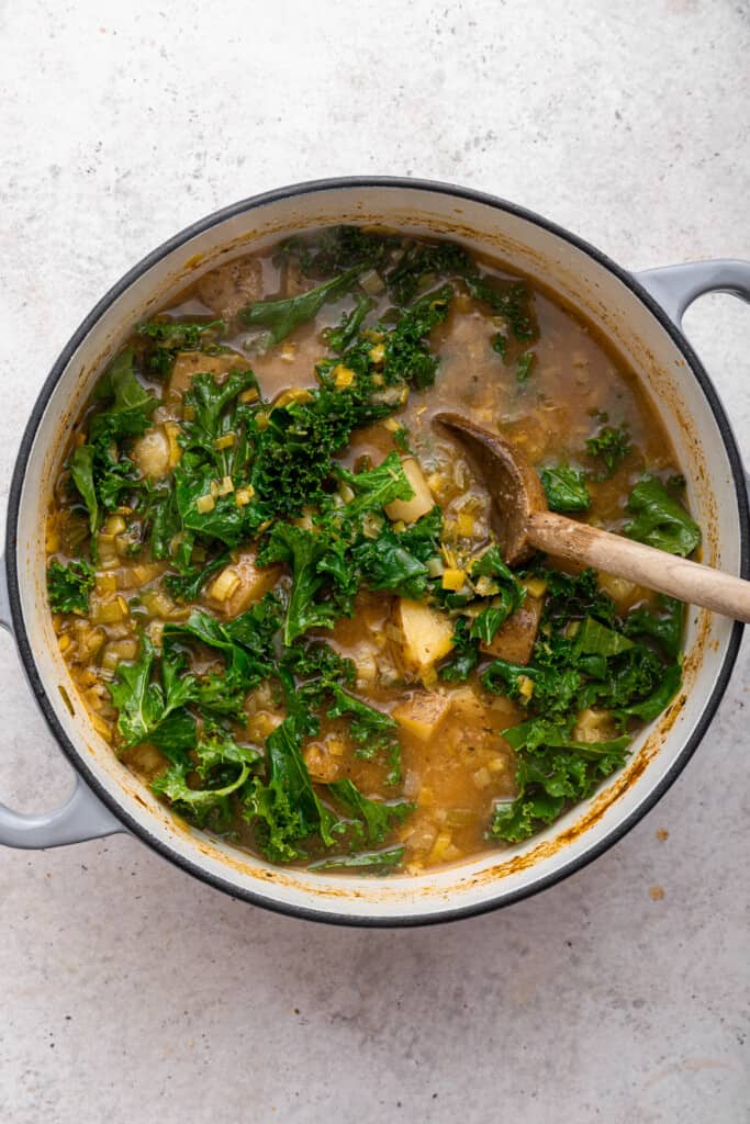 Wooden spoon stirring kale into soup