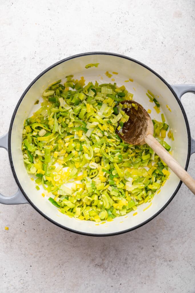 Overhead view of wooden spoon stirring leeks in pot