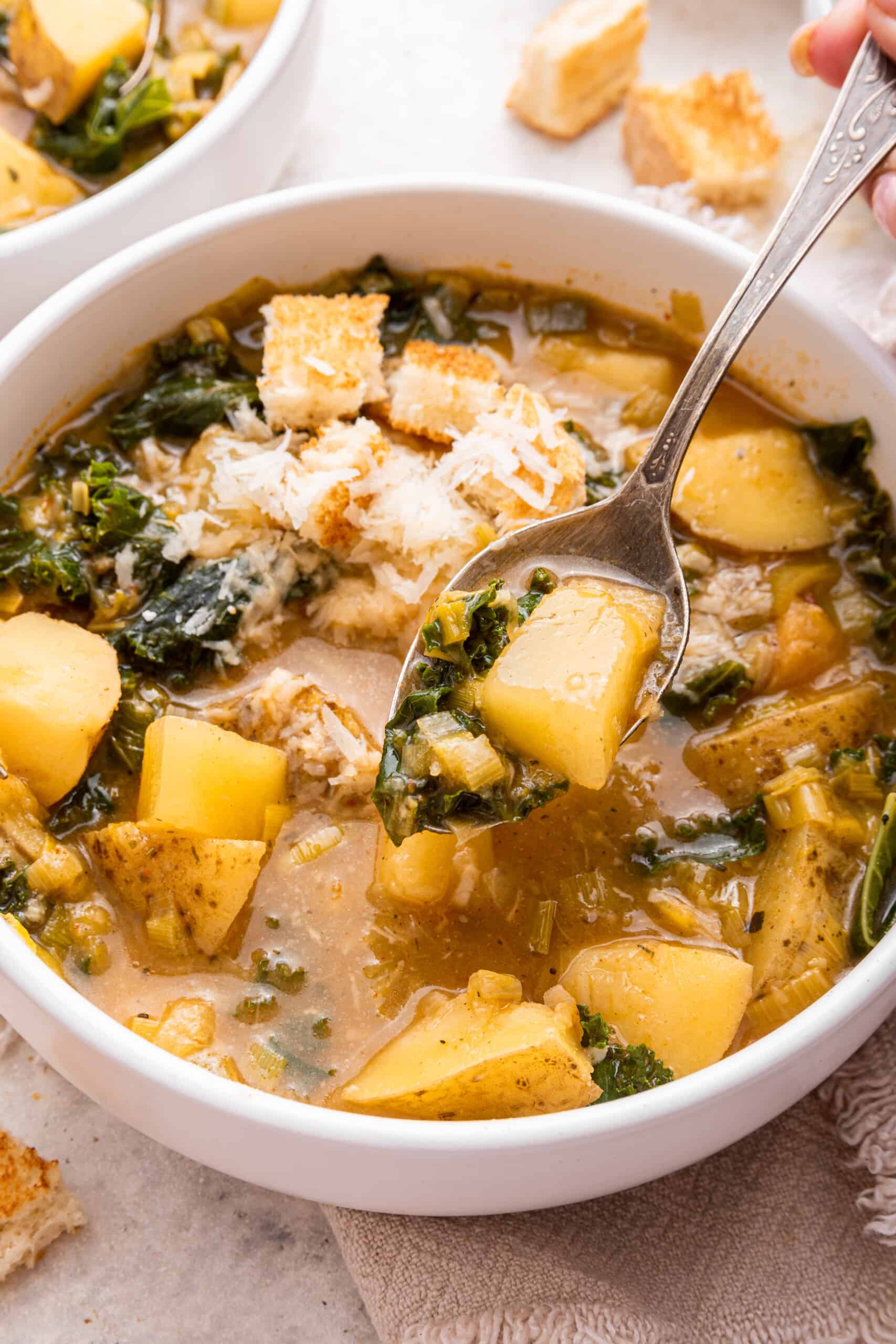 Bowl of chunky vegan potato soup, with spoonful of potato and kale
