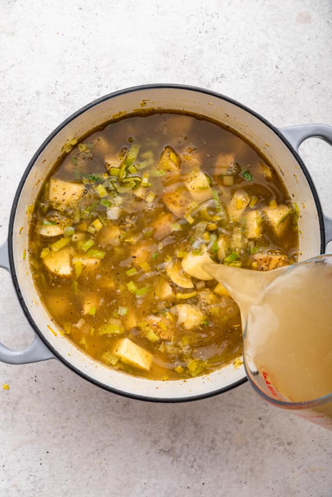 Pouring broth into pot of vegan potato soup