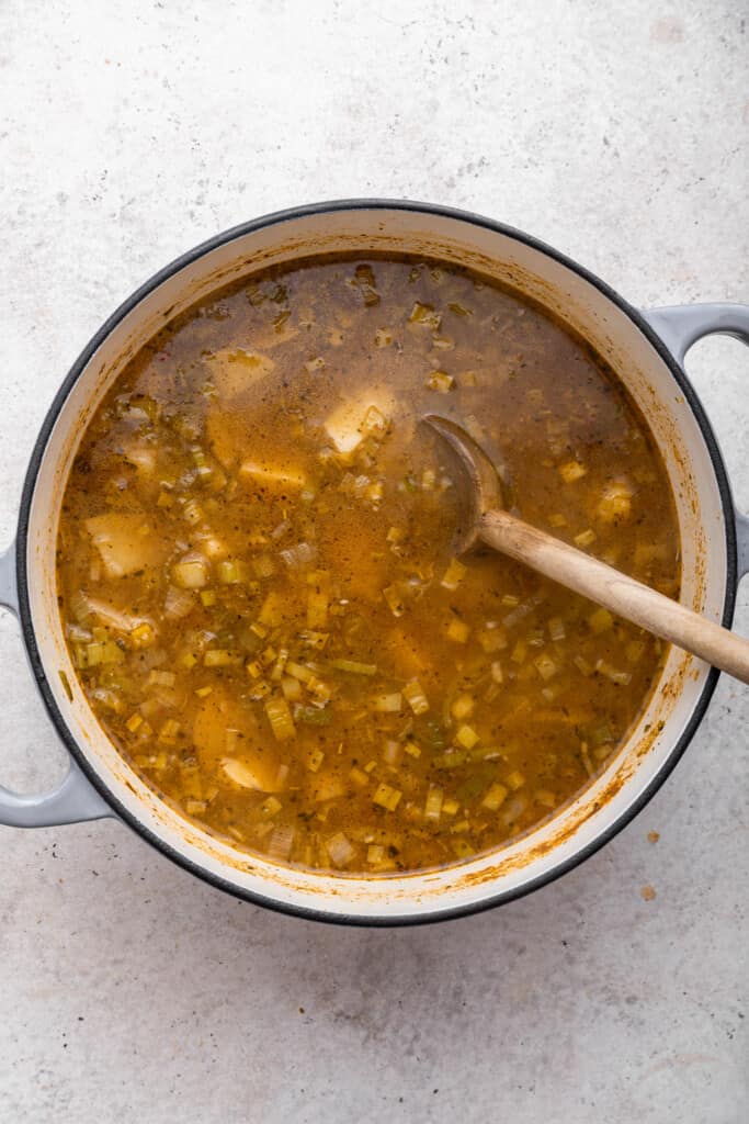 Wooden spoon stirring vegan potato soup in pot