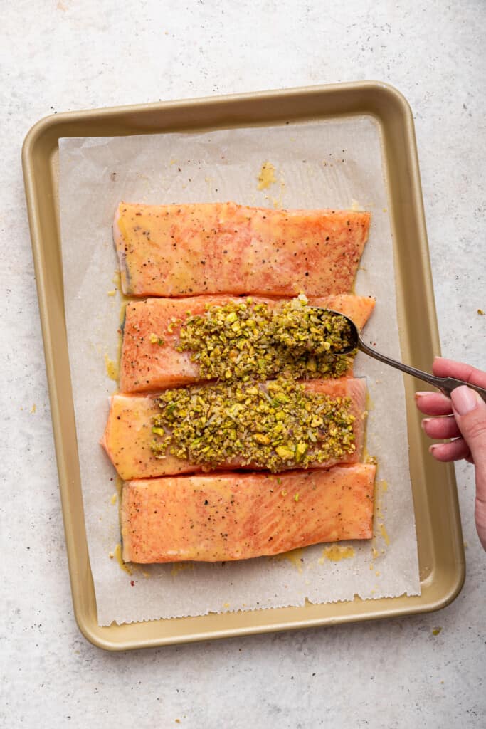 Spooning pistachio crust onto salmon fillets