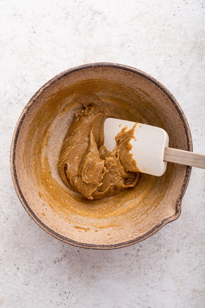 Overhead view of rubber spatula stirring bowl of wet ingredients for tahini cookies