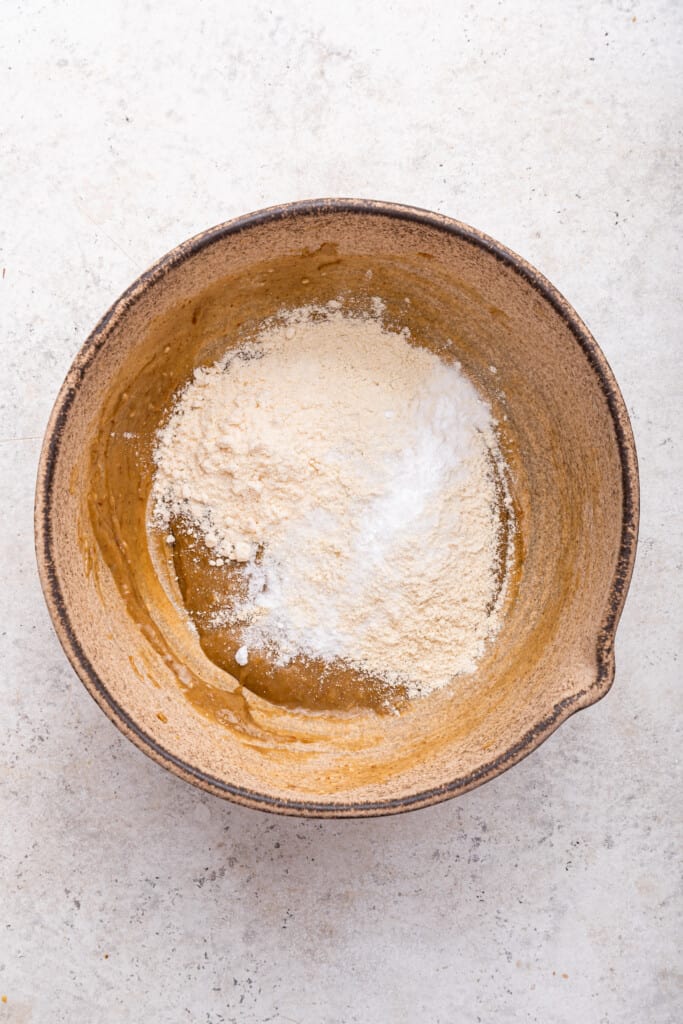 Overhead view of dry ingredients added to bowl of tahini chocolate chip cookie dough