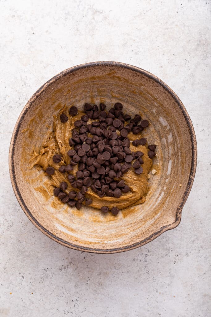 Overhead view of chocolate chips added to bowl of tahini cookie dough
