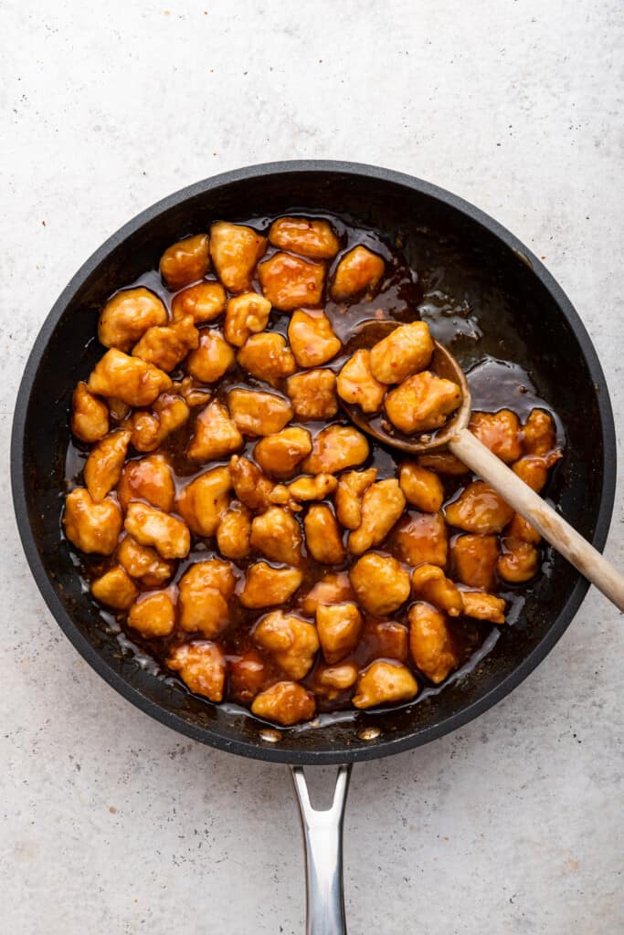 Overhead view of honey sriracha chicken in skillet with wooden spoon