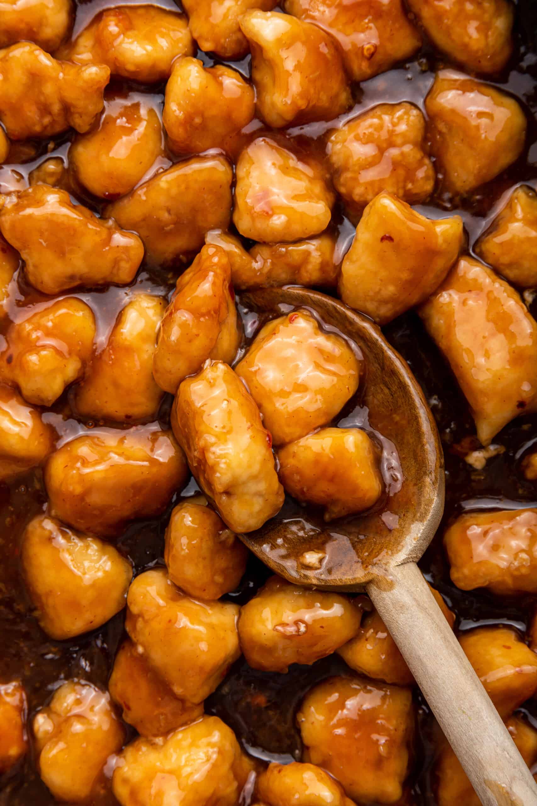 Wooden spoon lifting pieces of honey sriracha chicken from pan