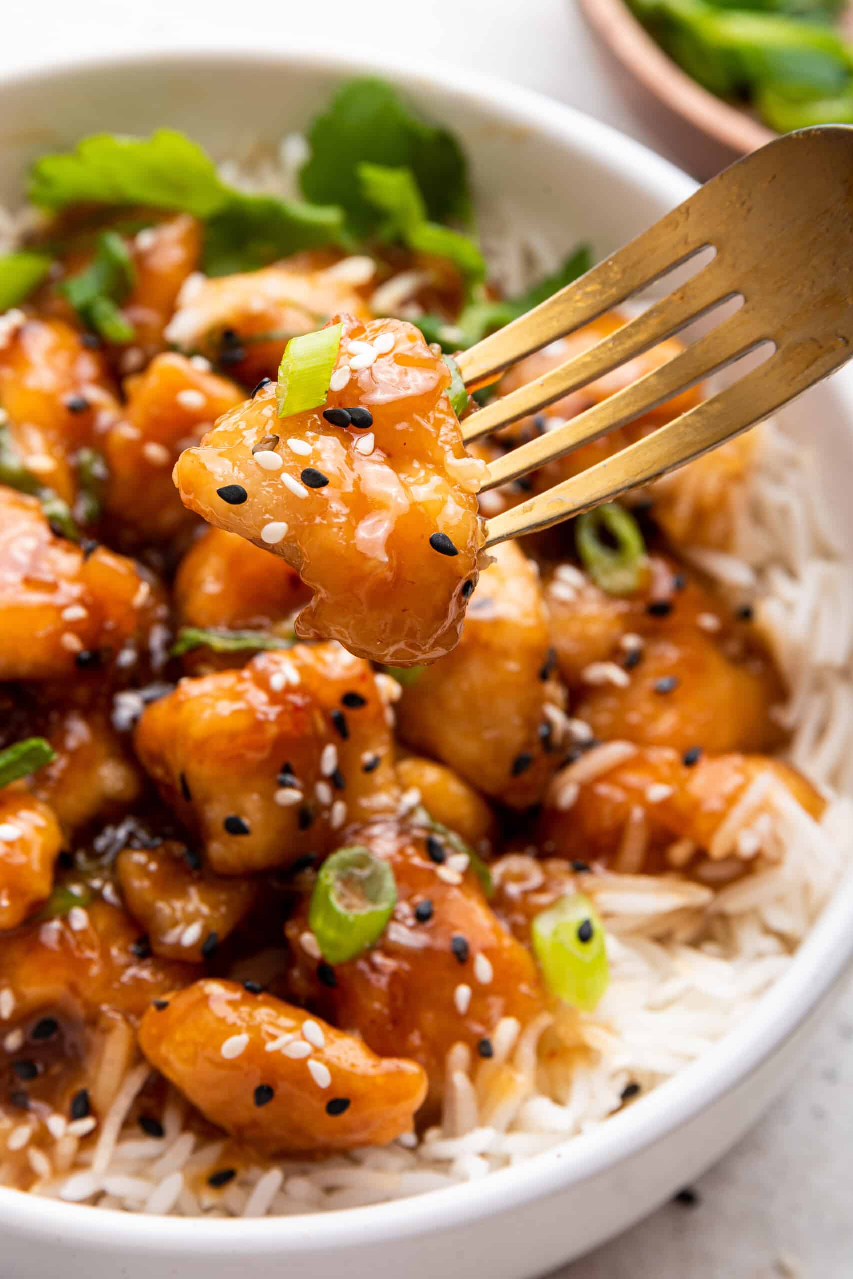 Fork holding piece of honey sriracha chicken over bowl