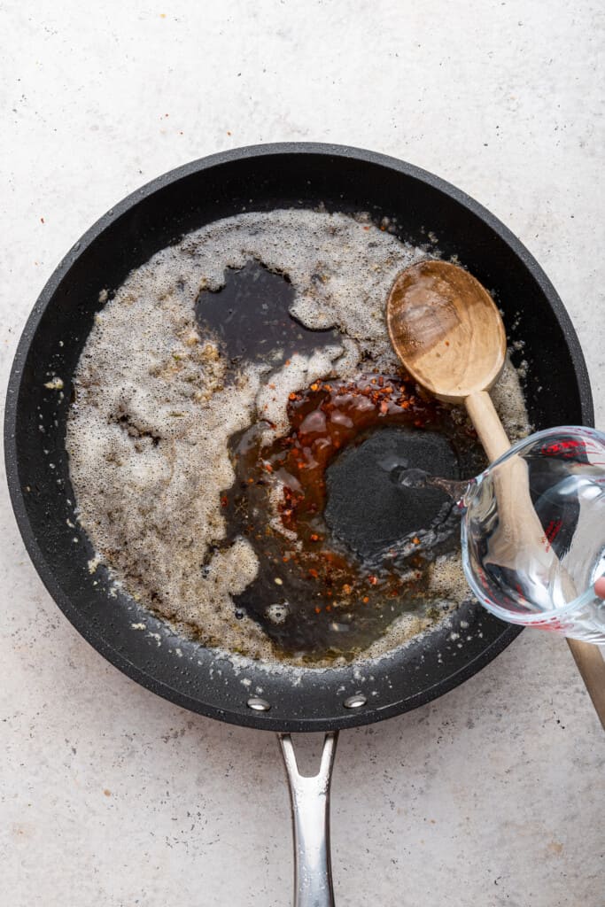 Pouring water into pan for sauce for honey sriracha chicken