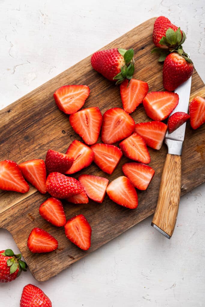 Overhead view of halved strawberries on cutting board with knife
