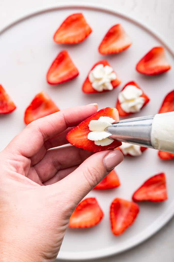 Hand holding strawberry while piping whipped cream on top