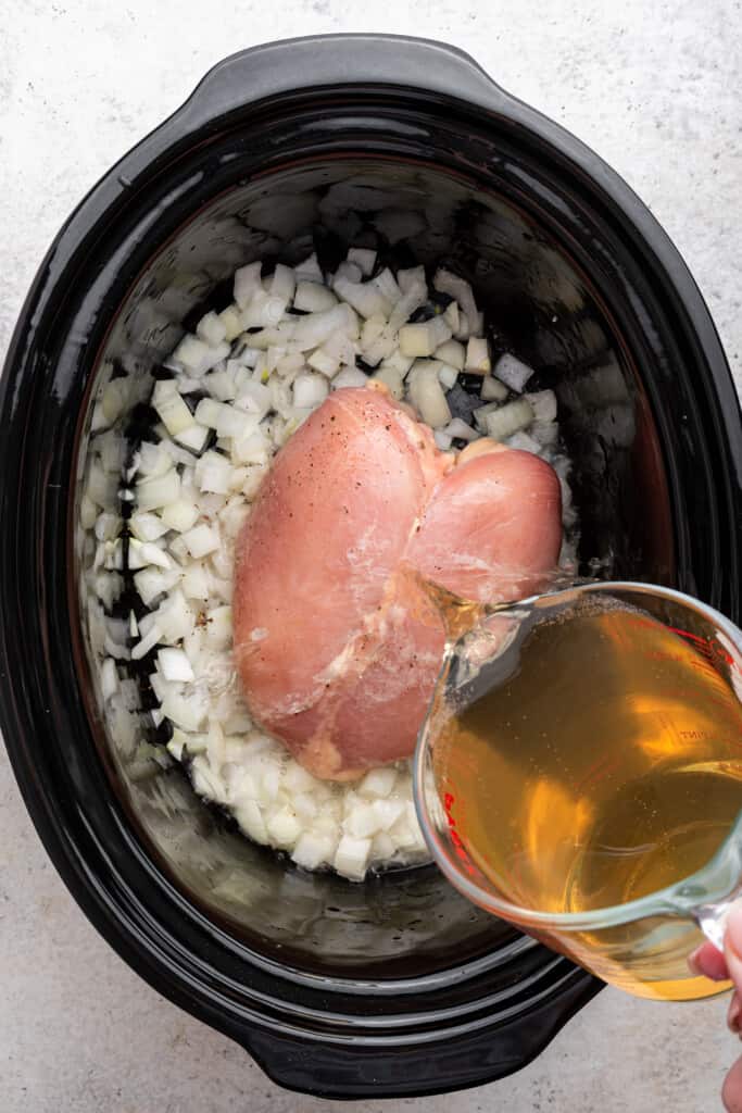 Pouring ginger ale into slow cooker with chicken and onions