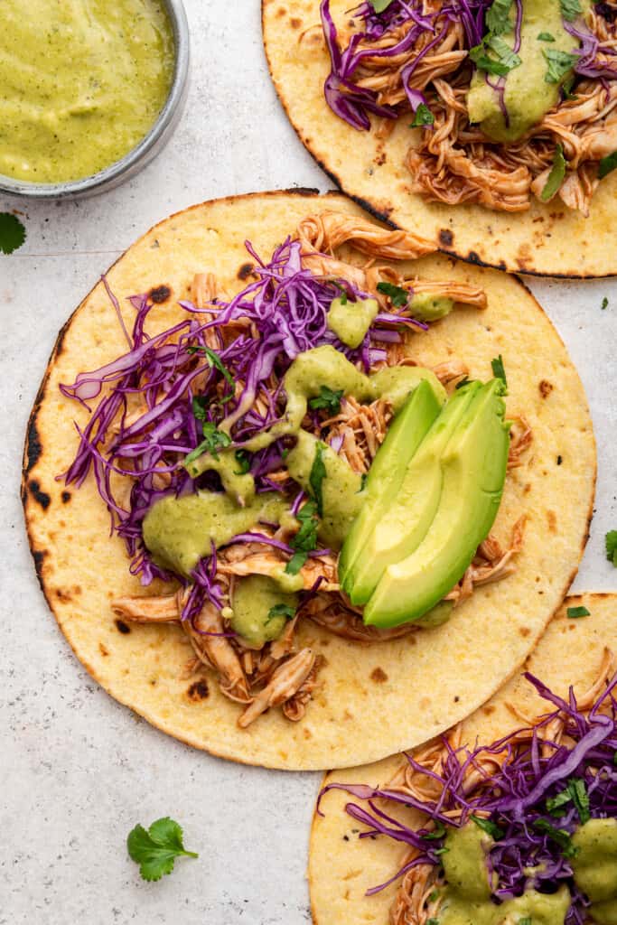 BBQ chicken tacos topped with tomatillo salsa, red cabbage, and avocado slices